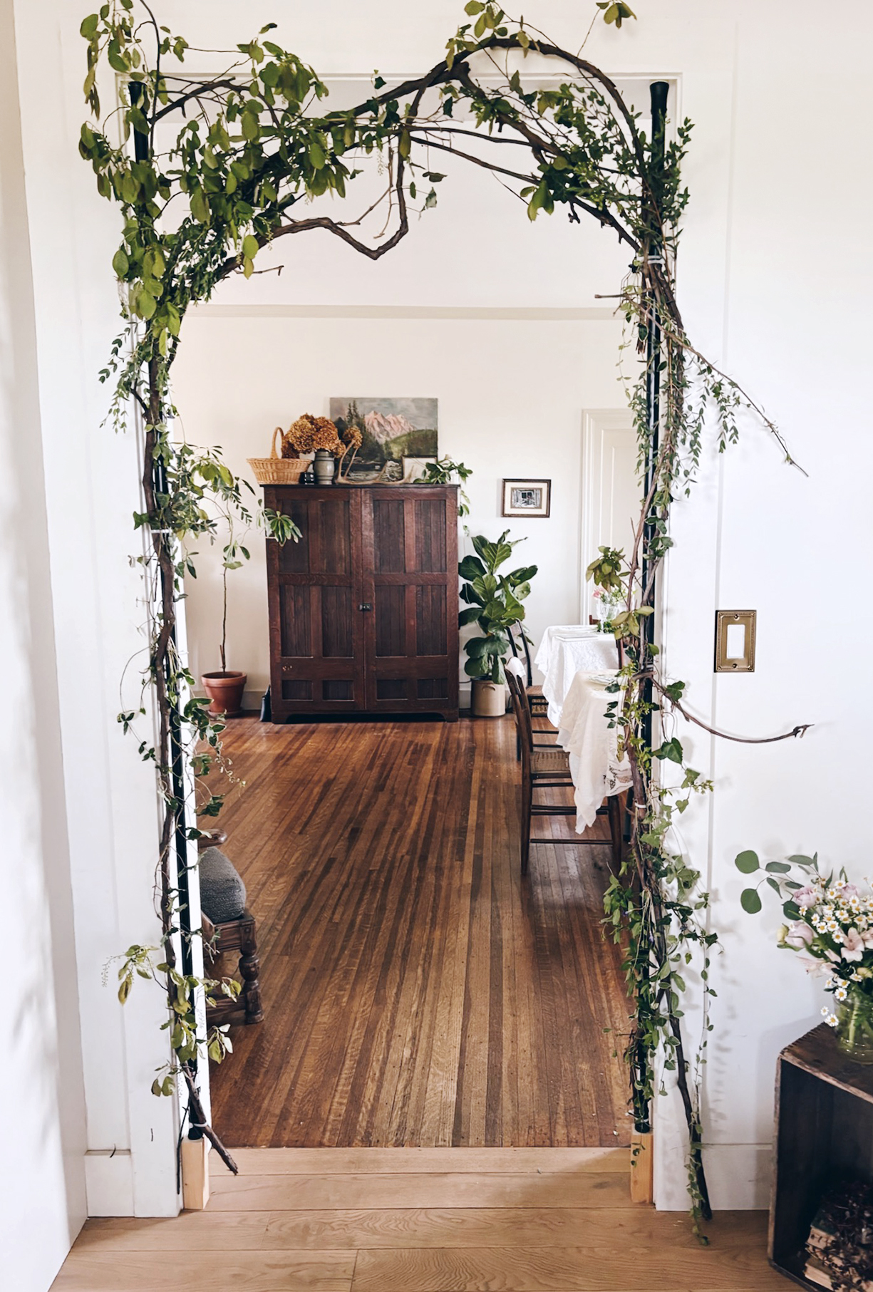 doorway with grapevine branches and greenery around it with antique cabinet seen through doorway of room